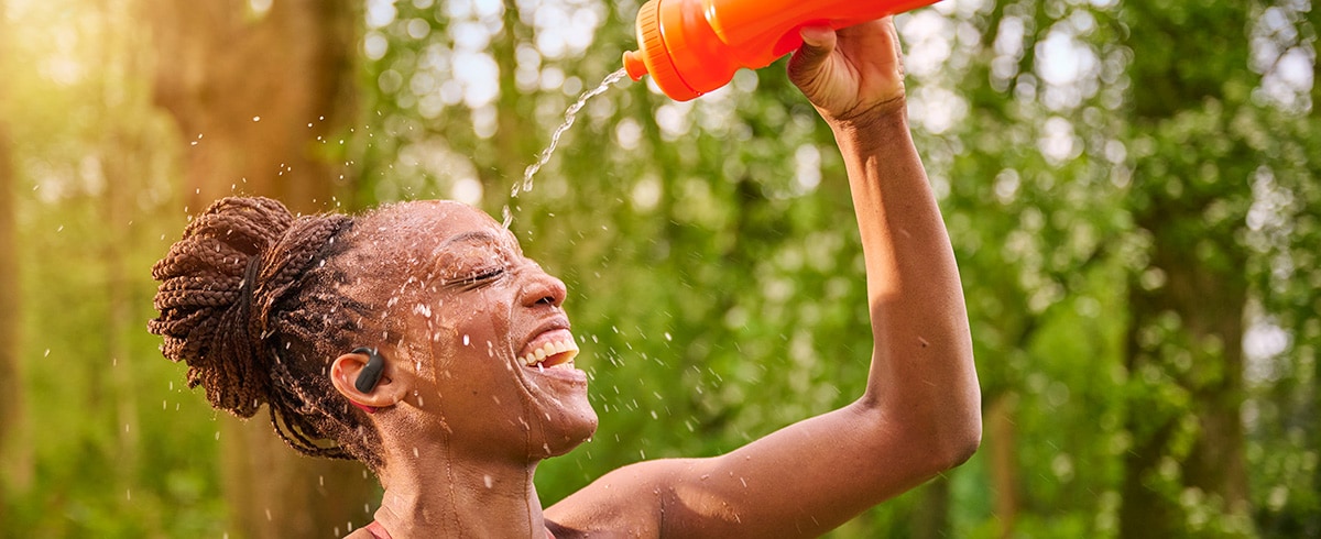 Vrouw die zich afkoelt door water over haar hoofd te gieten terwijl ze Philips sporthoofdtelefoon draagt in de buitenlucht